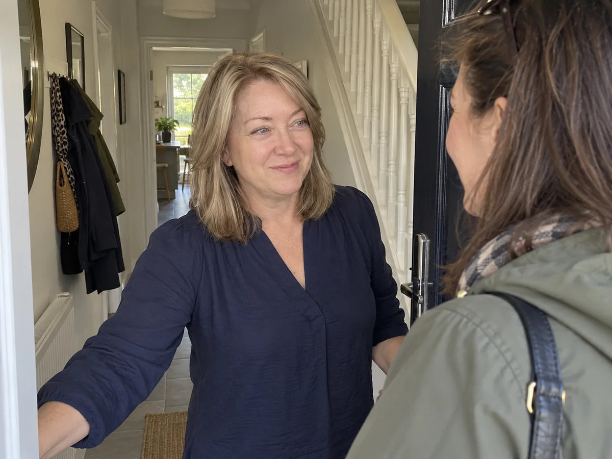 Illustrative scene of a woman welcoming a friend into her tidy hallway