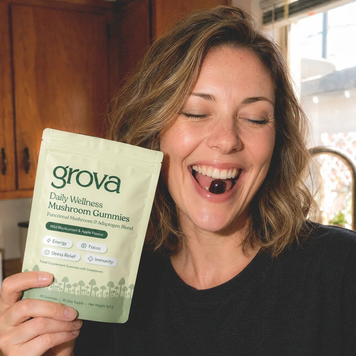 Woman holding a pouch of Grova Daily Wellness Mushroom Gummies while enjoying a gummy